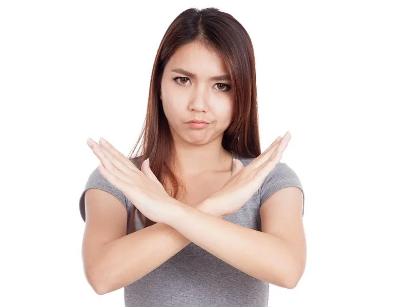Young woman with long brown hair stands with her arms crossed and hands open across her chest; she is clearly saying 'NO' with her body.