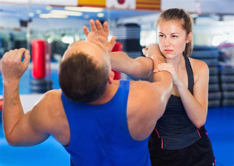 A woman in training gear is hitting the chin of a man with the heel of her hand. They are in a gymnasium; she is showing determination and resolve on her face.